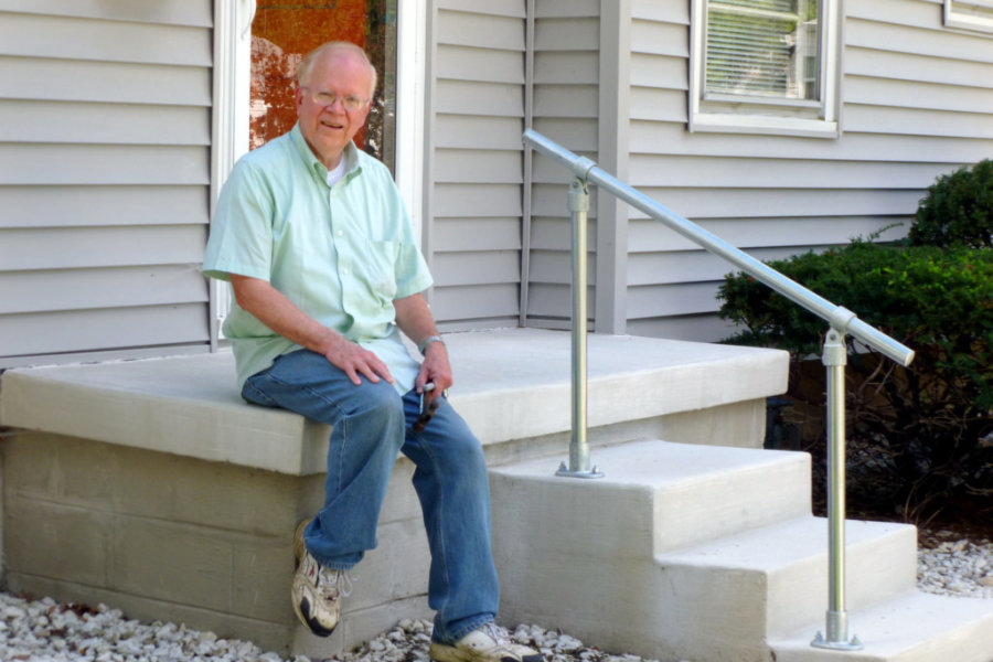 older man sitting on concrete steps with metal railing